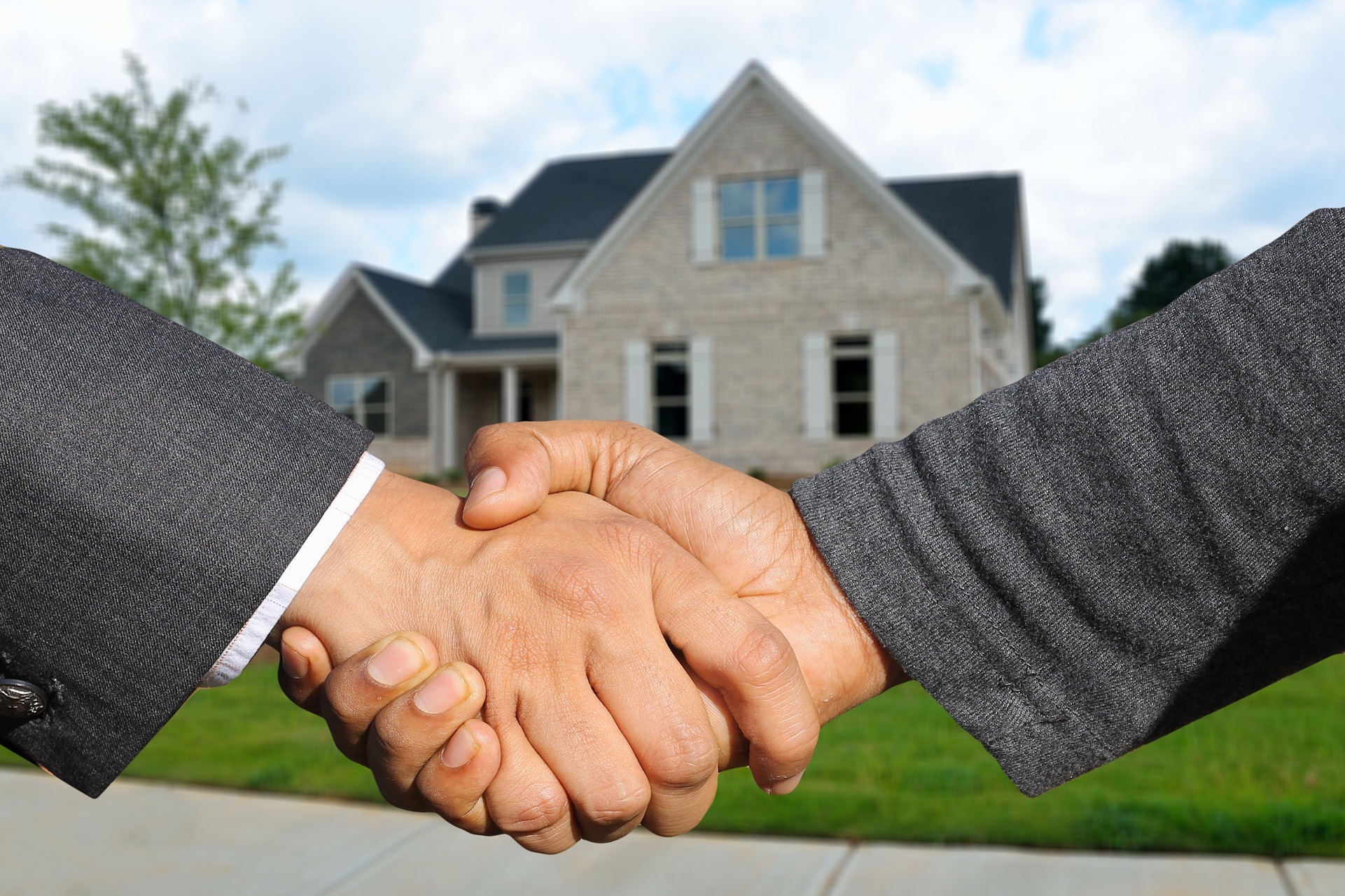 Real estate handshake two people shaking hands with a house in the background.
