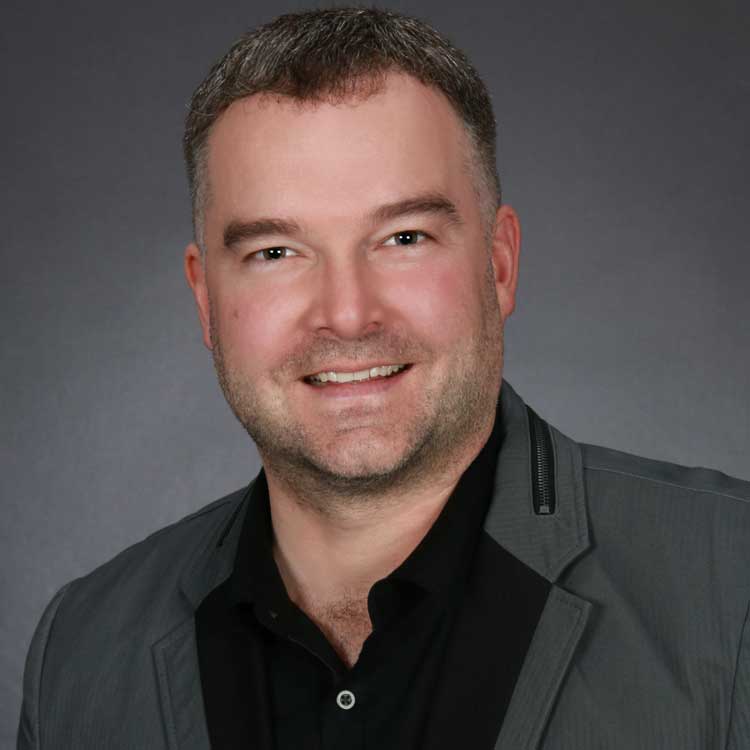 A portrait of a real estate agent in a black and grey suit smiling. 